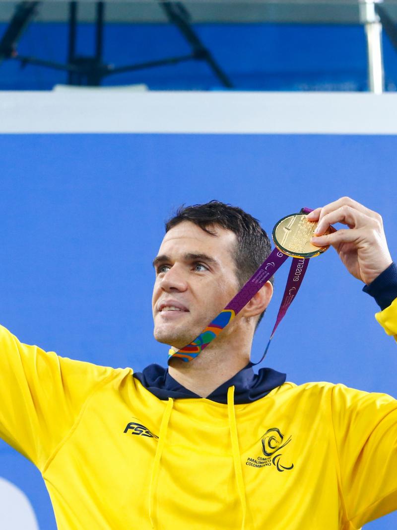 a male Para swimmer holds up his gold medal