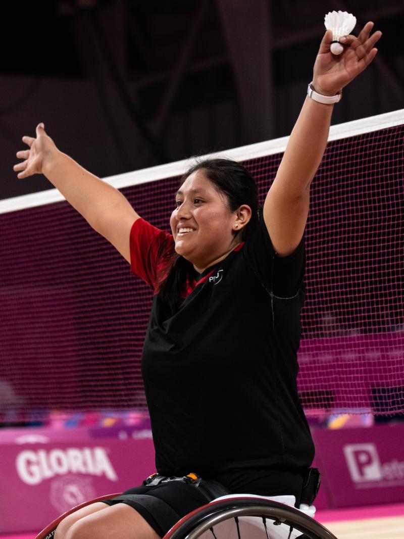 a female wheelchair badminton player throws her arms up in victory