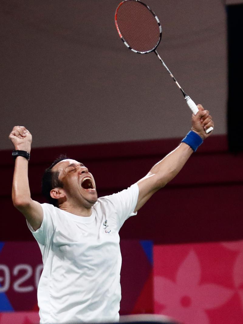 a male Para badminton player raises his fist and racquet into the air in celebration