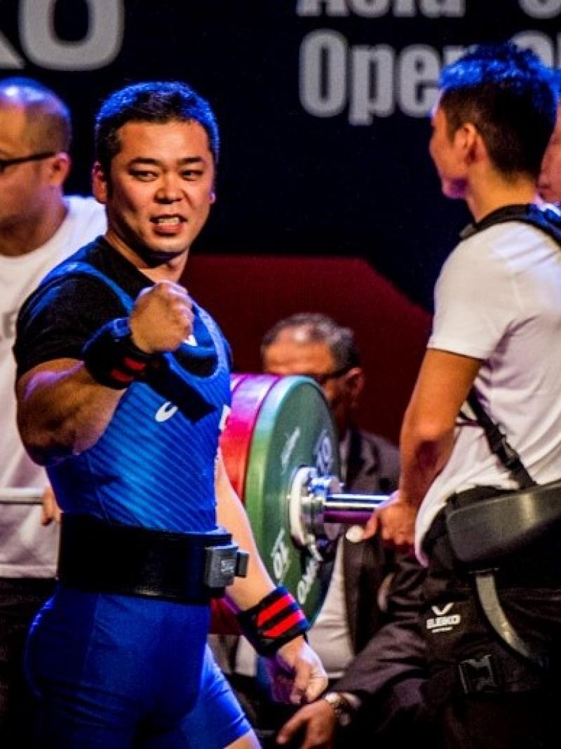 A male Para powerlifter celebrating with three assistants in the background