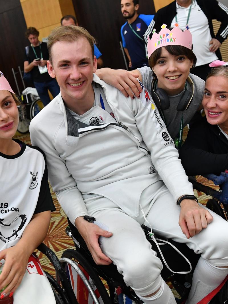 Male wheelchair fencer surrounded by friends for birthday