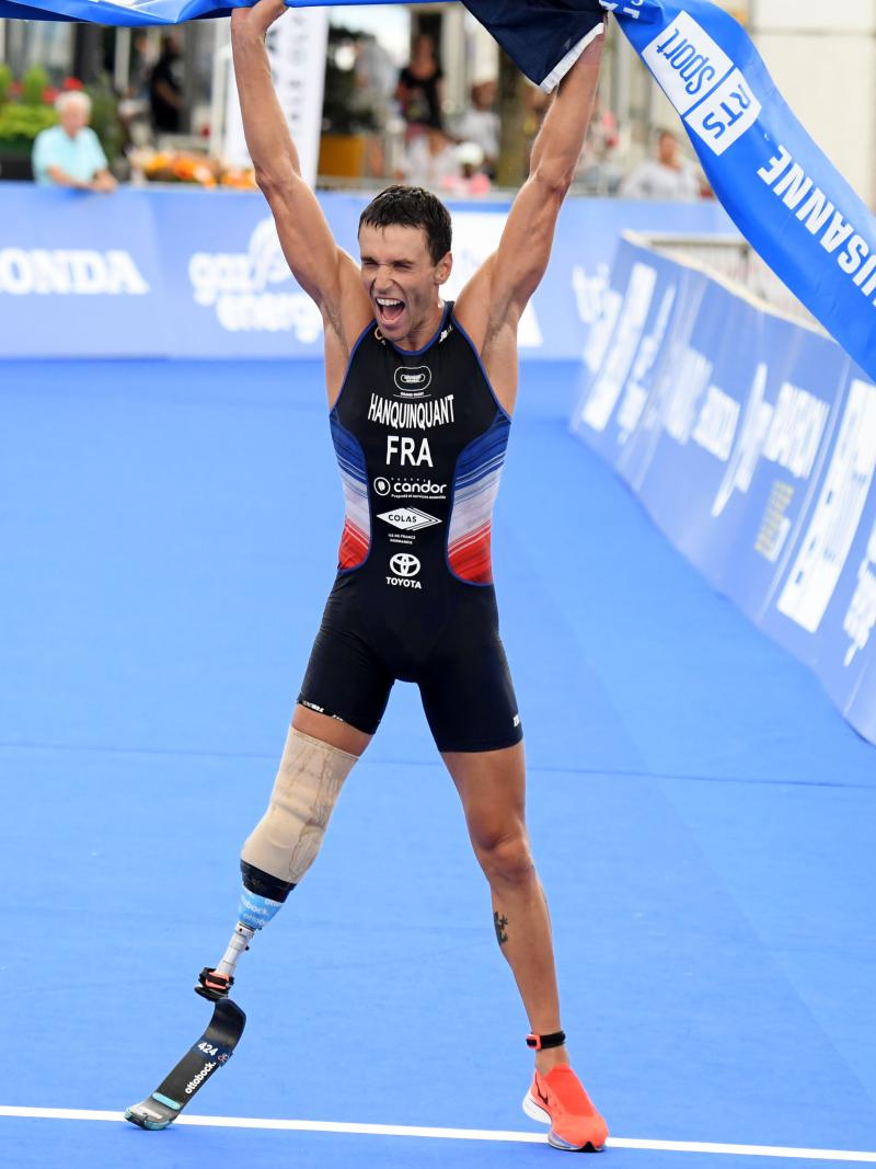 French man with right leg impairment lifts tape over head celebrating a win