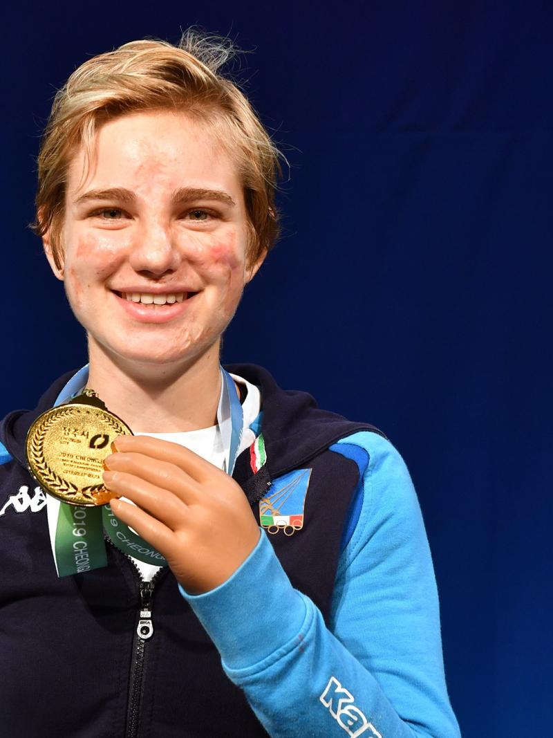 Female fencer smiles holding gold medal