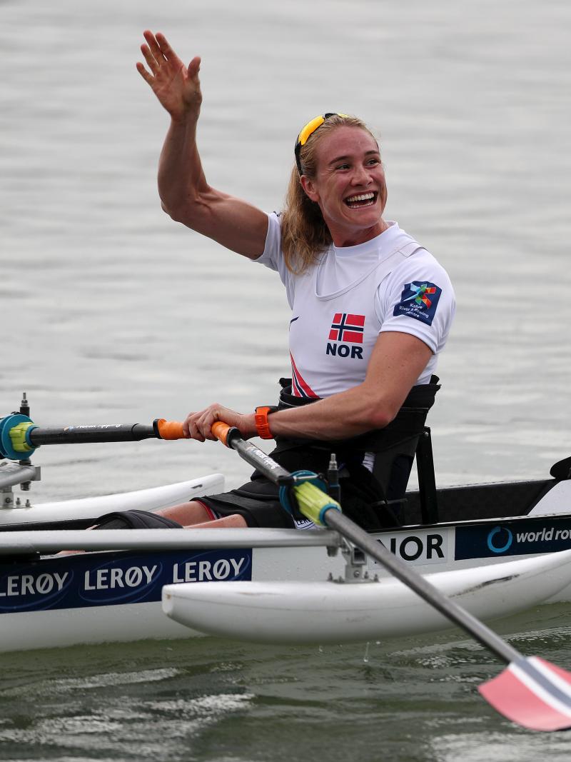 Woman in rowing boat waves at spectators