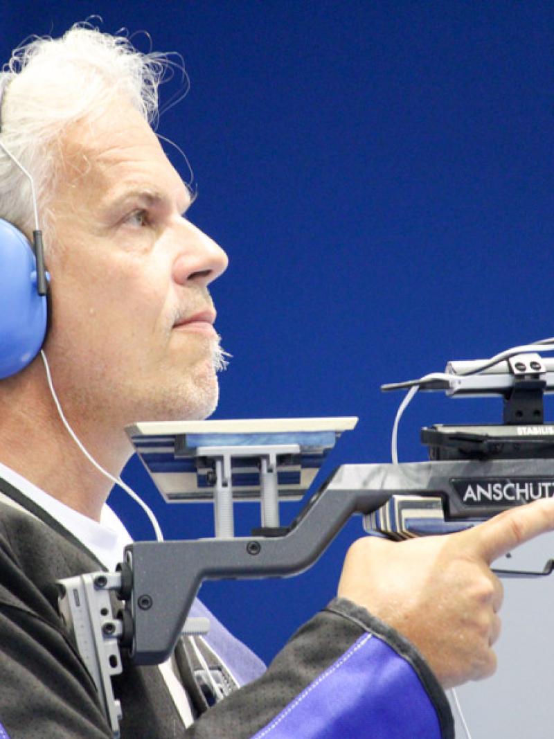 Male vision impaired rifle shooting athlete looks on with noise canceling ear protectors on