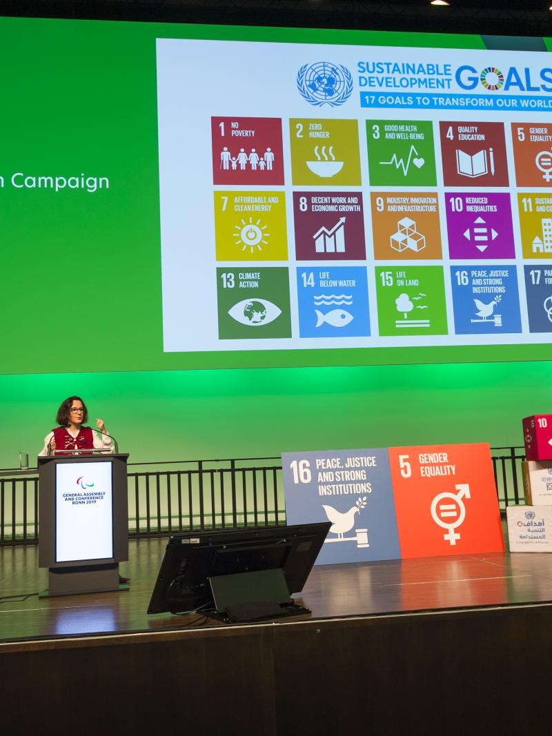 A woman on a stage making a presentation about the UN SDGs