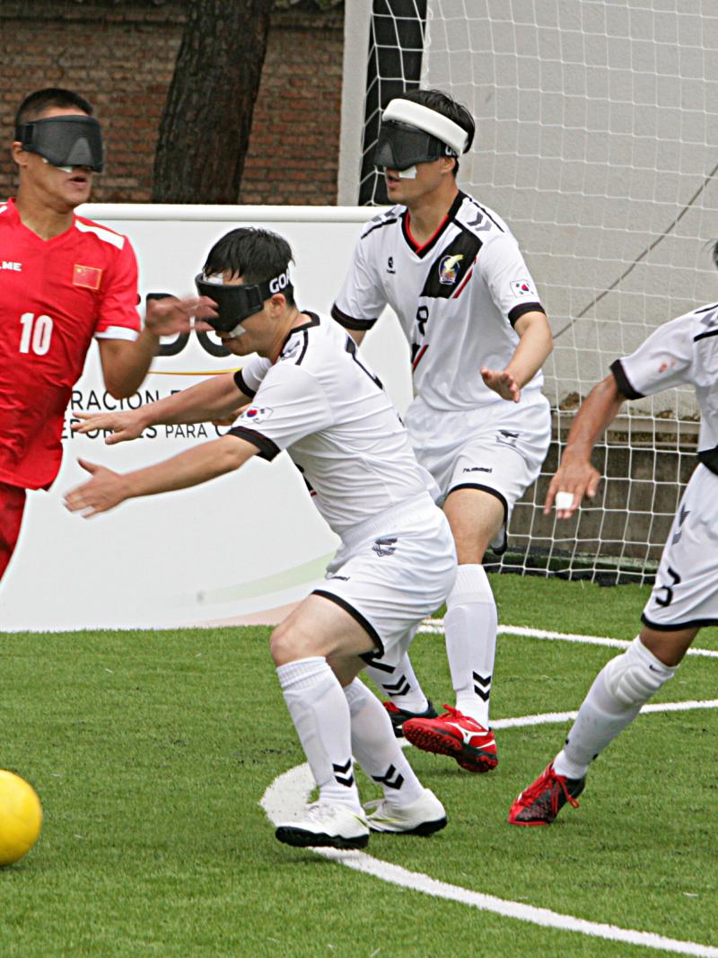blind football player taking the ball while defenders try to intercept him