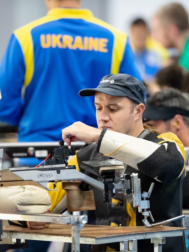 A man loading his rifle during a shooting competition with other competitors and a man standing next to him