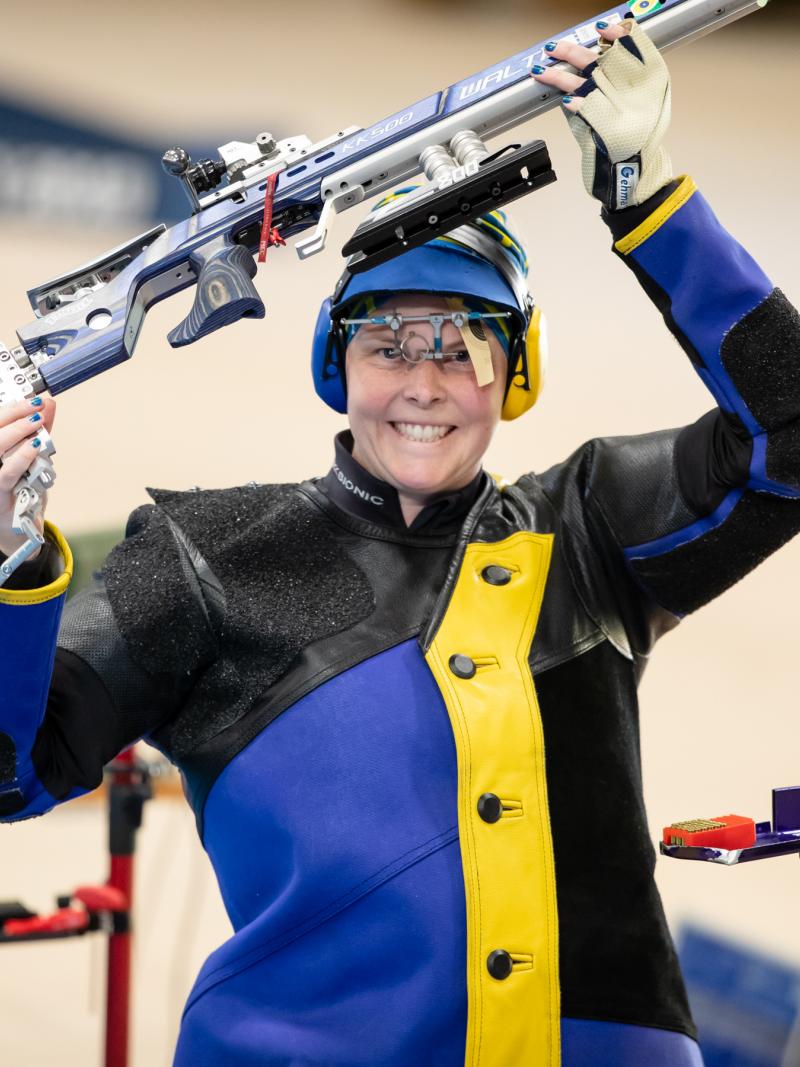 A female shooter smiling a holding her rifle above her head