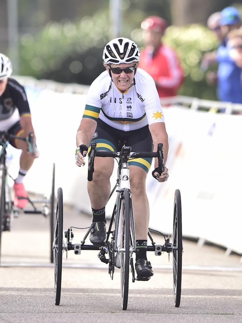 Australian woman in tricycle sprints toward finish line with opponent behind her