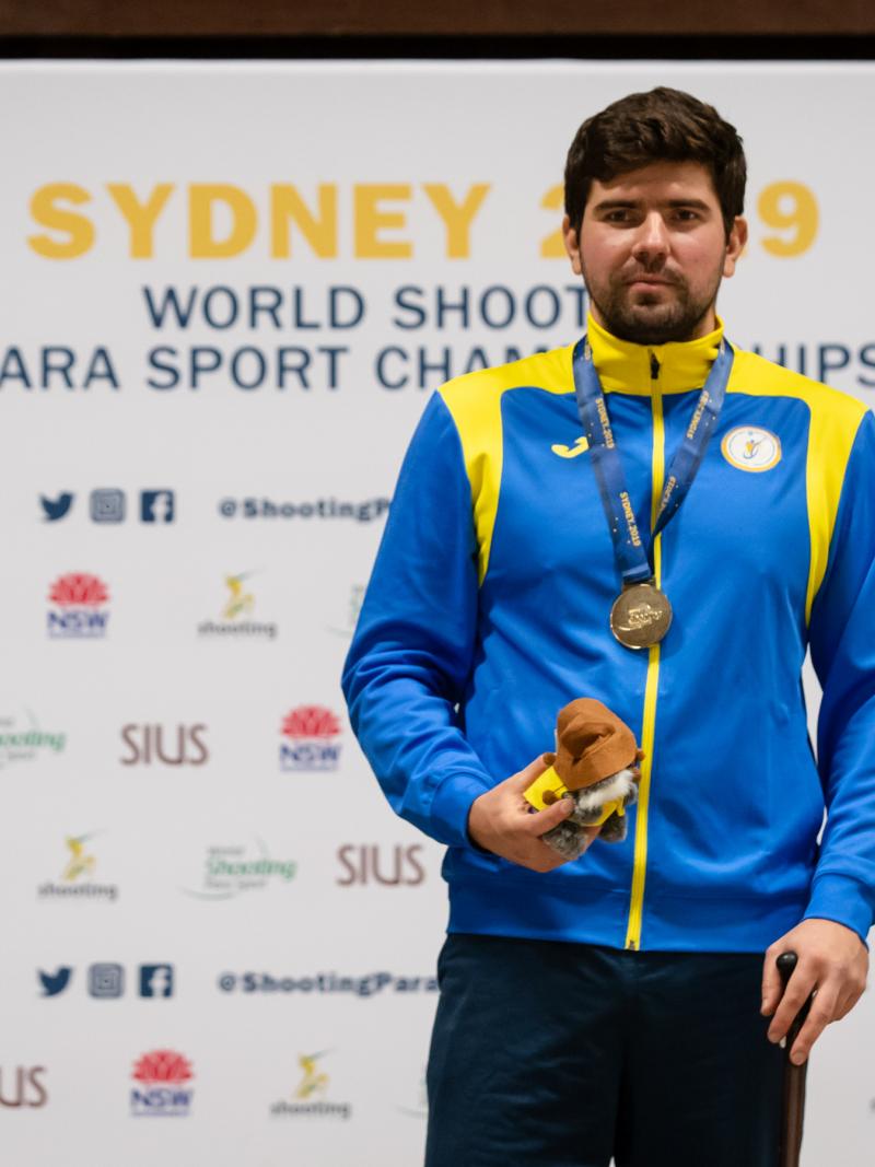 Ukrainian man stands with gold medal around neck and prize in hand