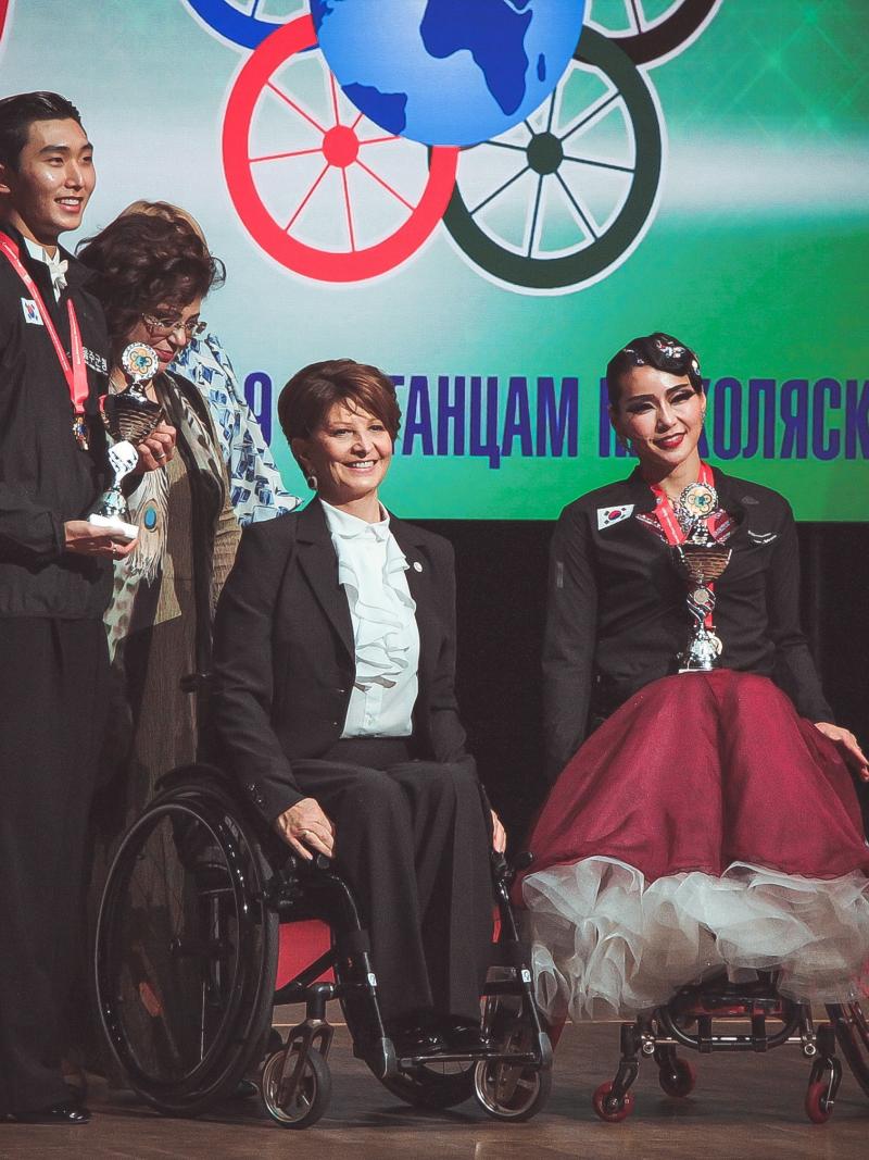 Female dancer in wheelchair and male standing partner on stage with award