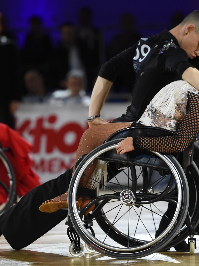 Standing male dancer dips his female wheelchair dancer