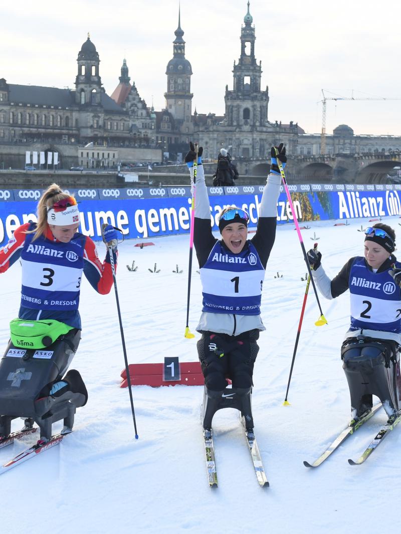 A female sit-skier celebrating between two other skiers