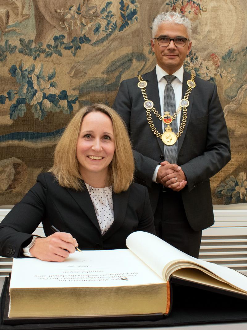 Female German athlete in wheelchair signing a book with mayo standing behind