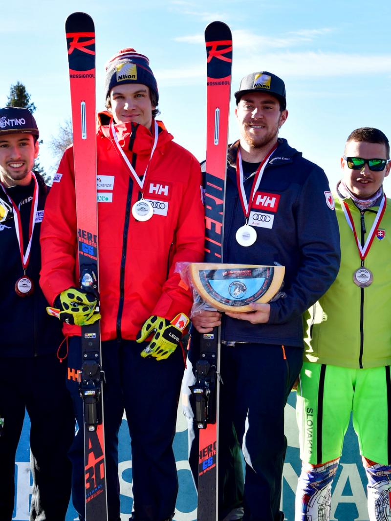 Three vision impaired male skiers with their guides pose on a podium