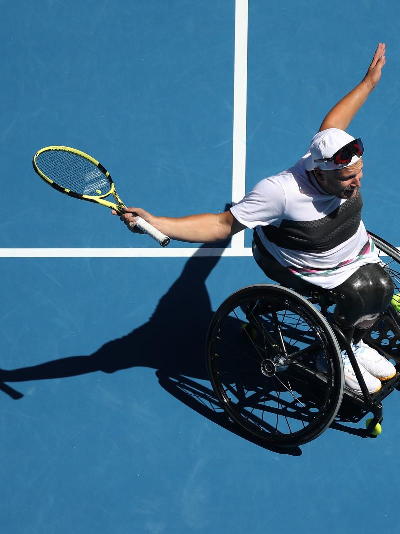 Dylan Alcott on the court extending his arms in celebration while holding the racket