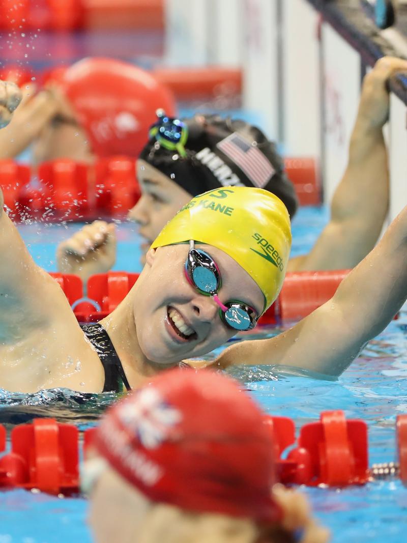 A female Para swimmer celebrating with your hand in the air between two other swimmers