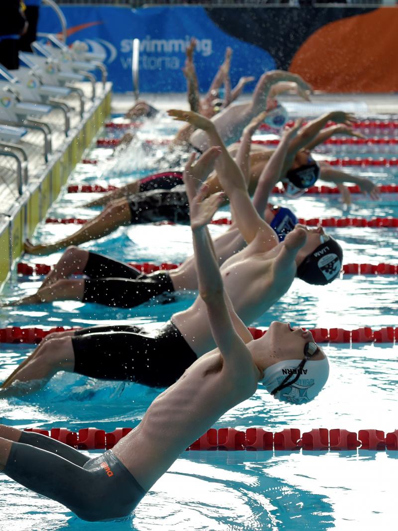 A group of male swimmers jumping in the water for a backstroke race