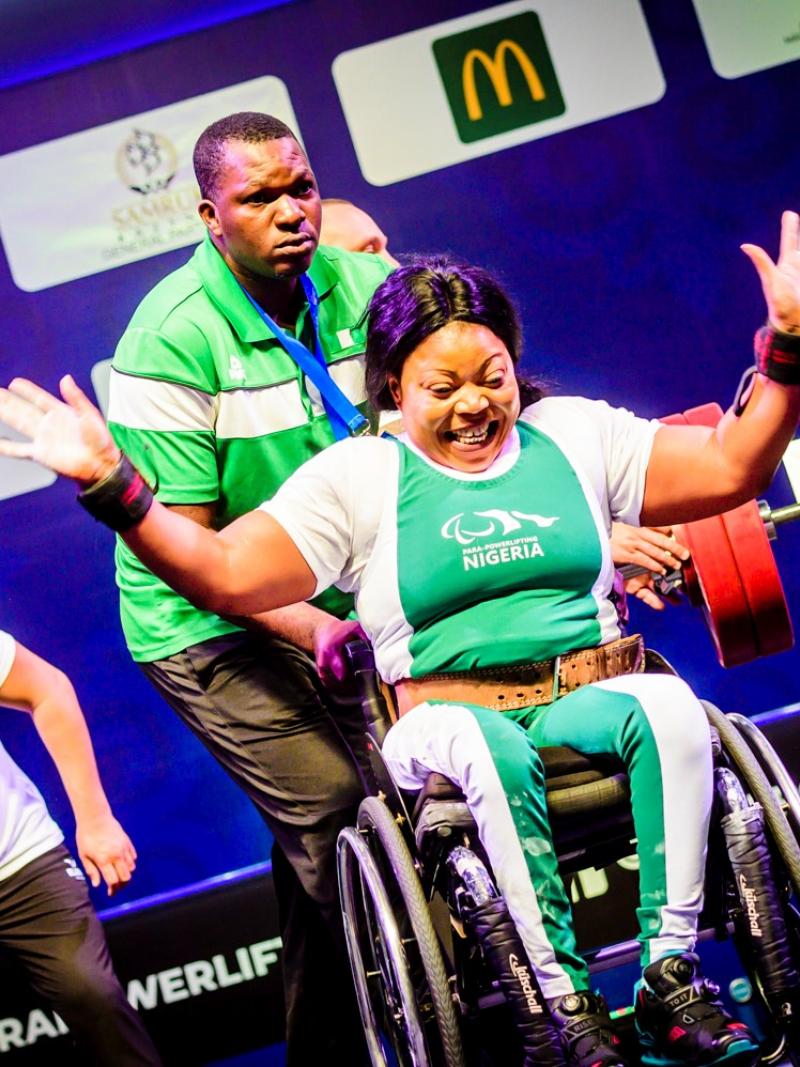 A woman in a wheelchair celebrating with a man standing behind her during a Para powerlifting competition