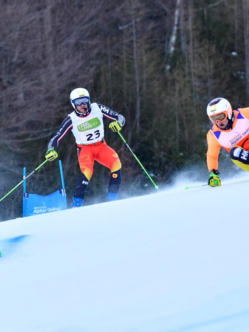 Male alpine skier making a turn with his guide behind him