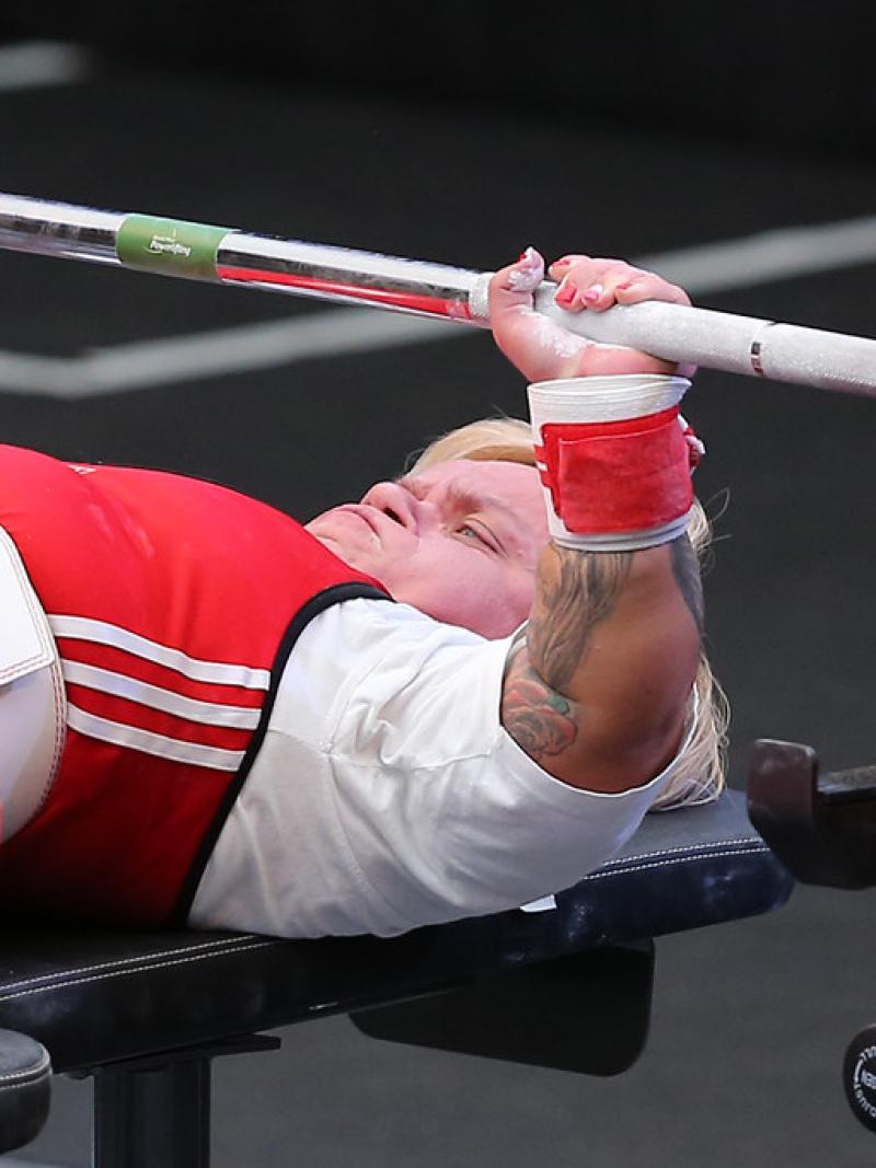 A female Para powerlifter with a red outfit preparing to lift the bar