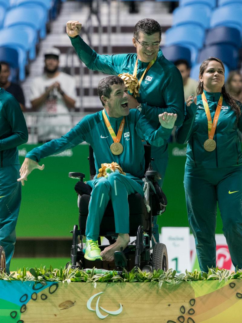 Six people on a podium. Three are in wheelchairs, three are standing behind them