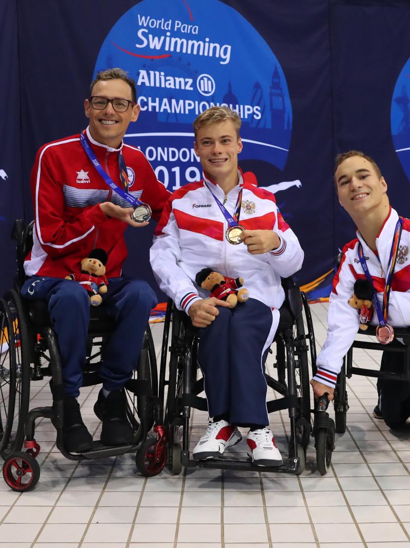 Three men in wheelchairs showing their medals