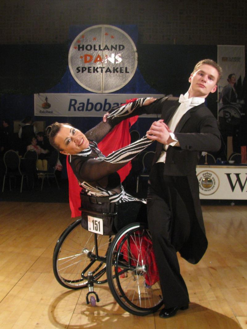 A standing man dancing with a woman in a wheelchair