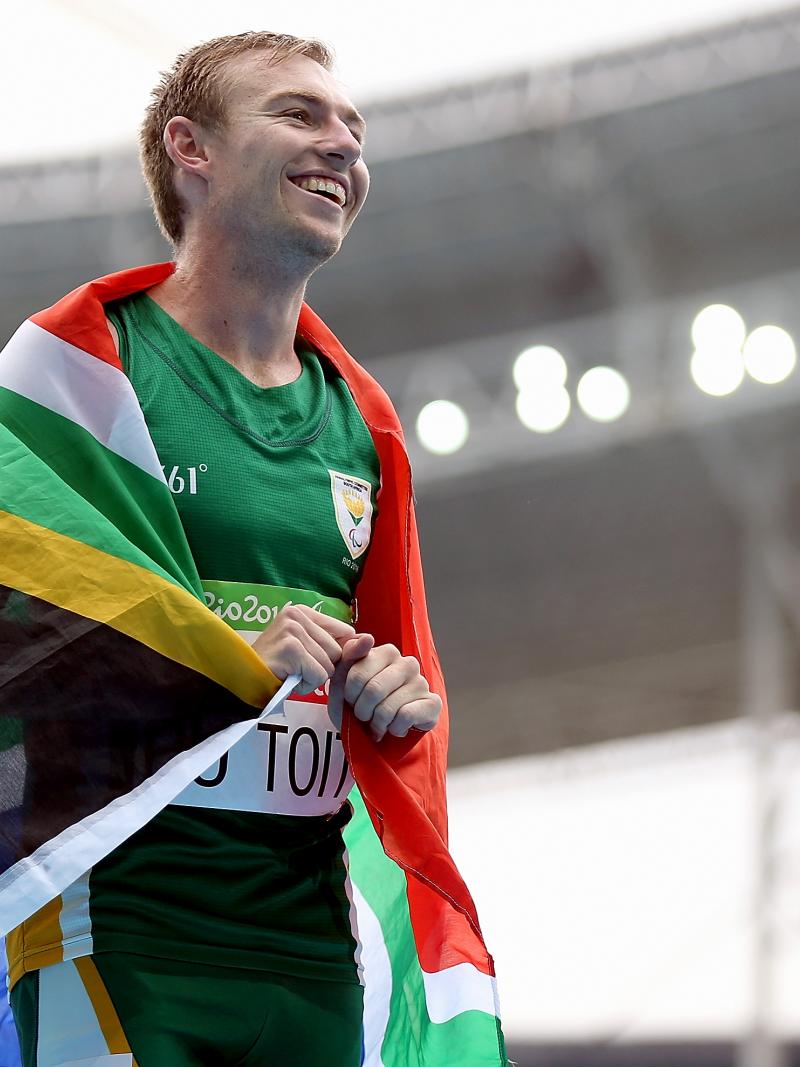 A smiling man with the flag of South Africa around his shoulders 