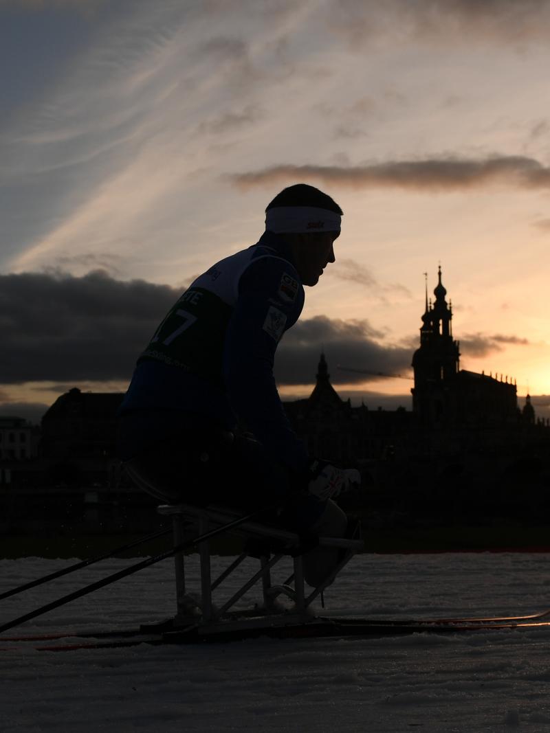 A male sit-skier competing on the snow with the Dresden skyline as background