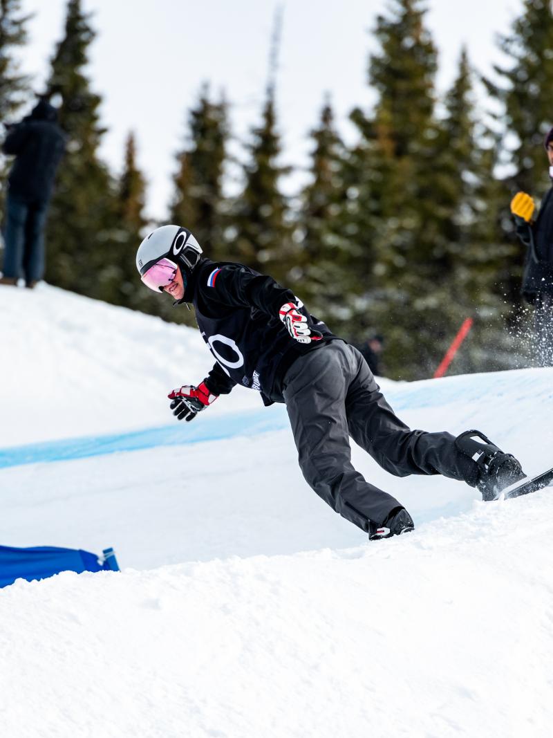 A male Para snowboarder competing being observed by three people