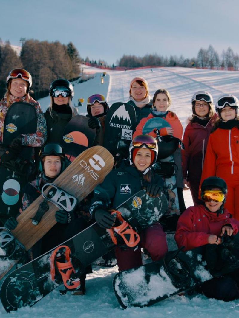 A group of 12 female Para snowboarders posing for picture with their equipment on the snow