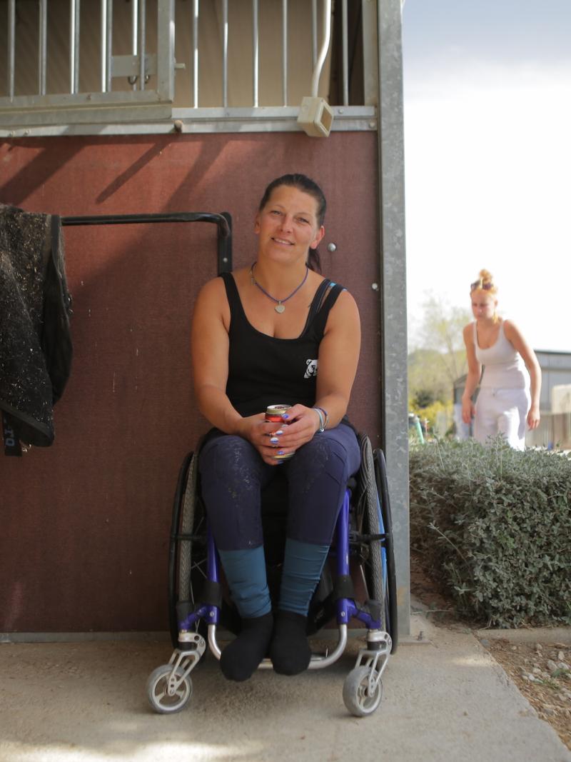 Woman in wheelchair smiles outside a horse stable