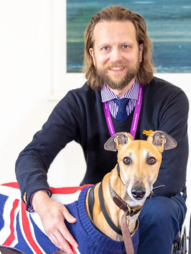 Male wheelchair user poses with his dog in a UK flag sweater