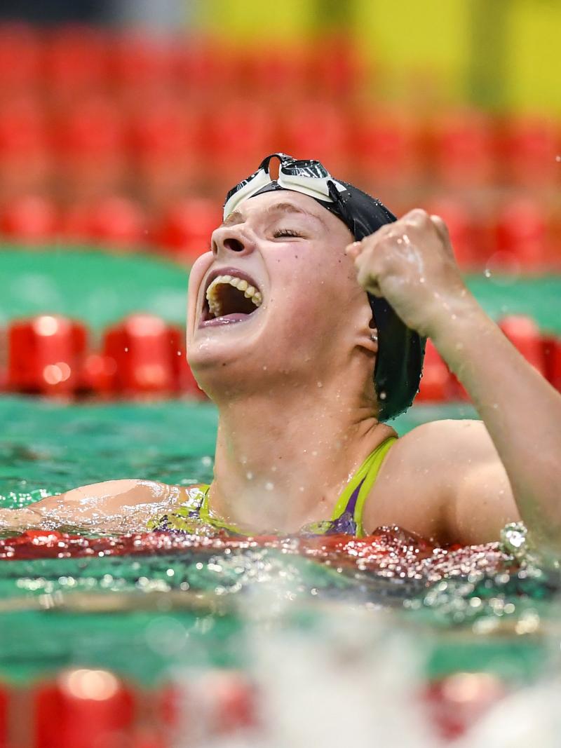 A female swimmer celebrating in the water in front of another athlete