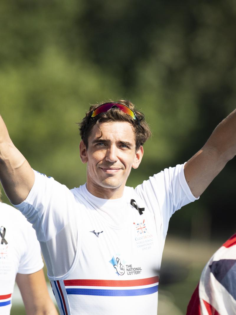 Male British rower smiles with both arms raised