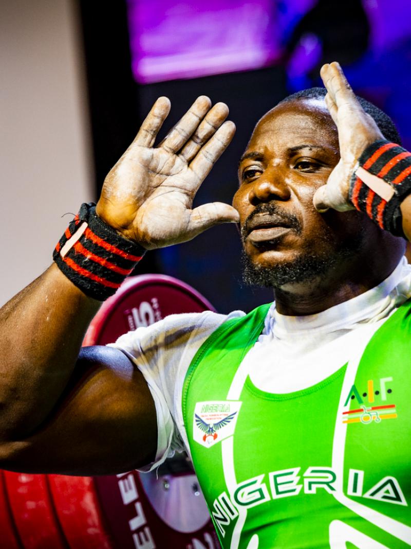 A male powerlifter with his hands in front of the face and a bar with discs behind him