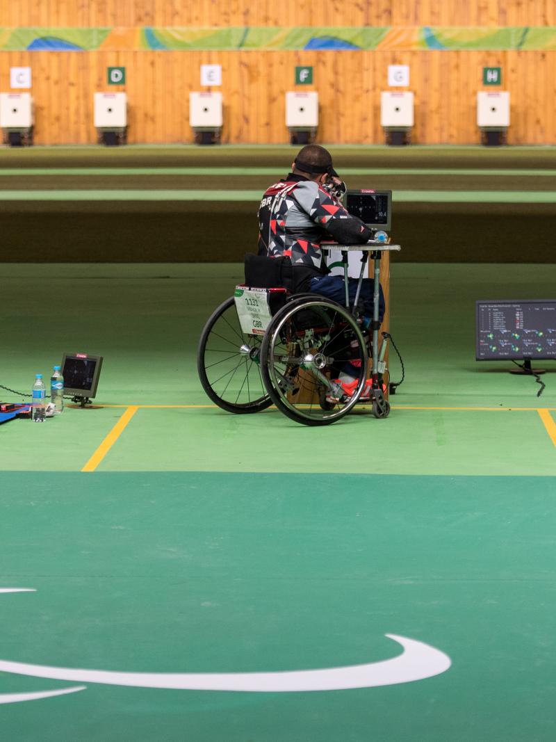 A man on the floor and two persons in wheelchairs with rifles aiming at targets in a shooting Para sport competition