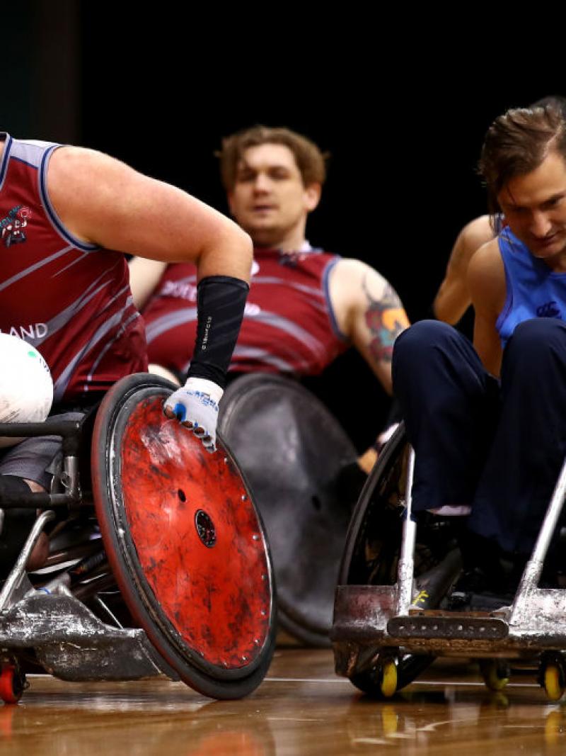 Male wheelchair rugby player moves with ball in his lap