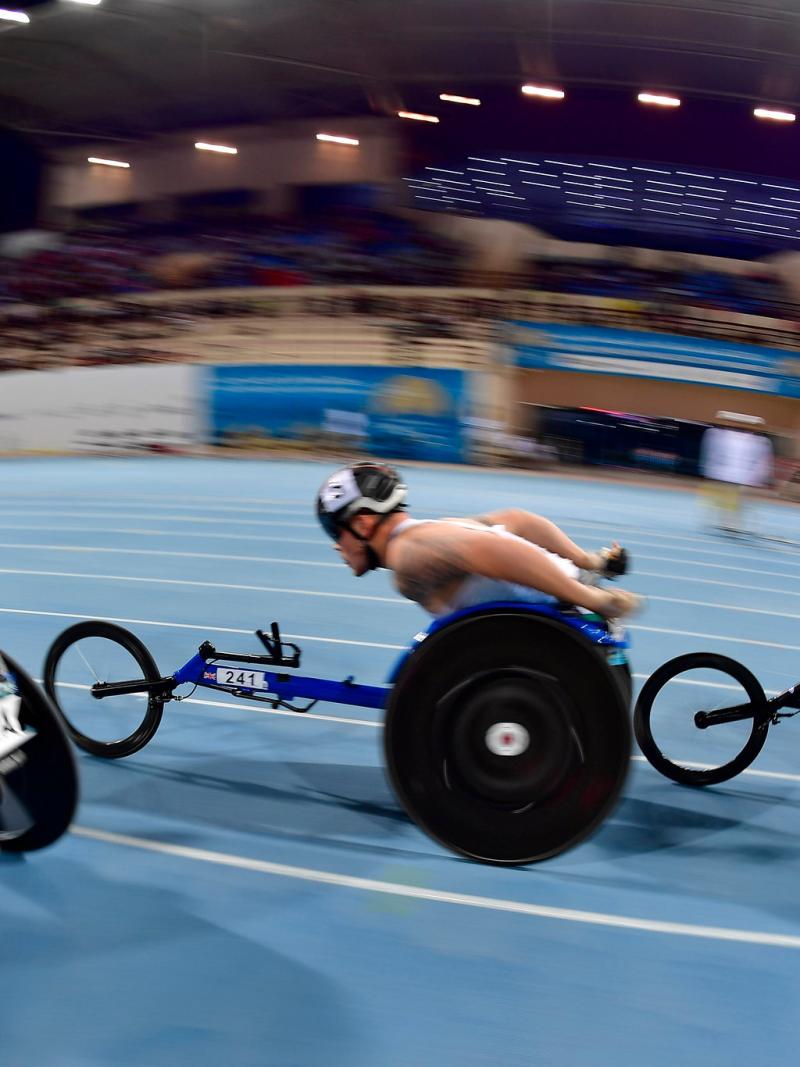 Three men in racing wheelchairs competing in a blue track