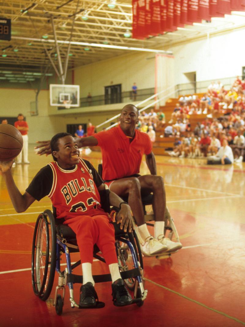 Boy in wheelchair holds basketball while Michael Jordan tries to block