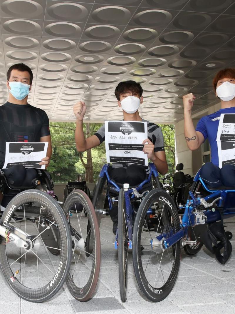 Five Korea wheelchair racers hold fists up with signs supporting Black Lives Matter