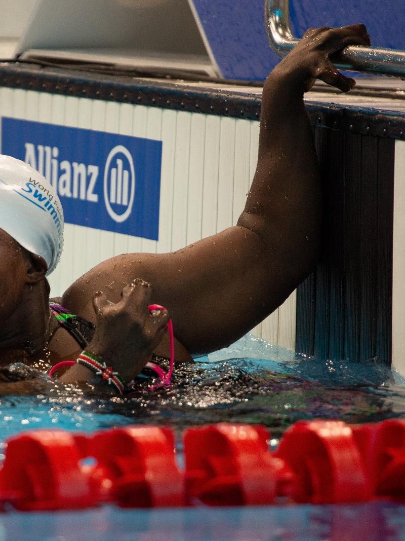 A female swimmer with her left hand on the board looking towards the pool