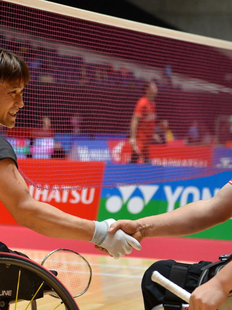 Two male Asian badminton players in wheelchairs shake hands