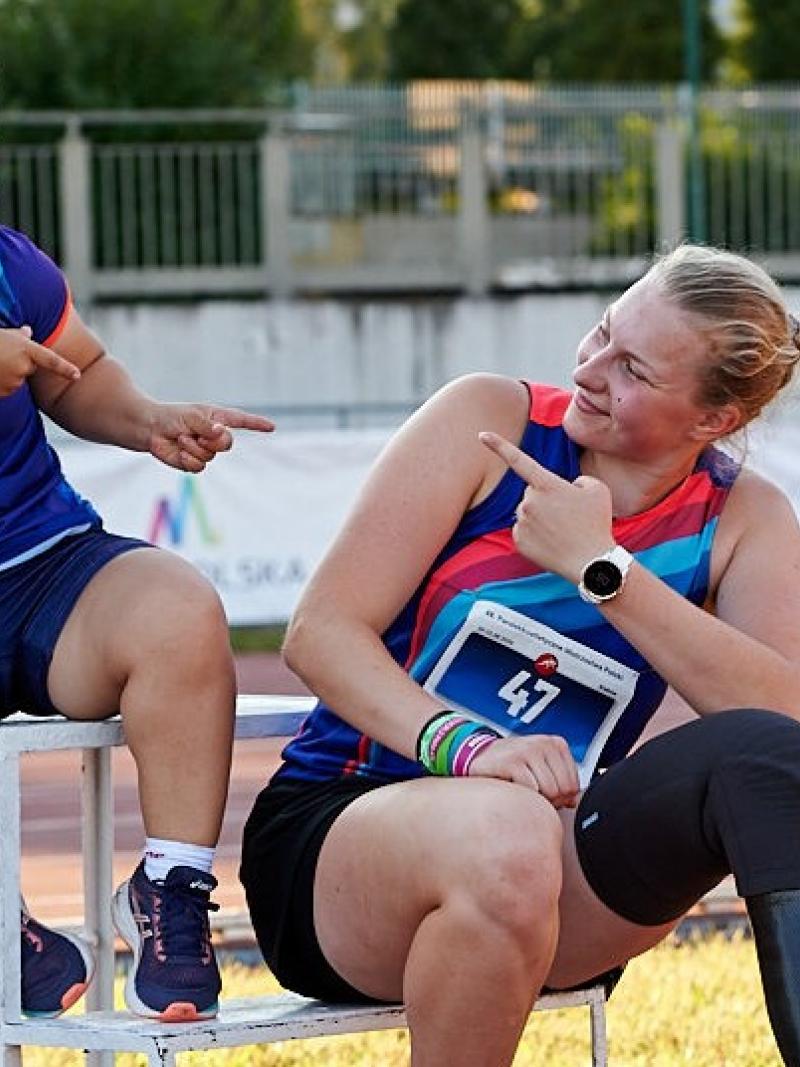 A short stature woman and a woman with a prosthetic leg point at each other