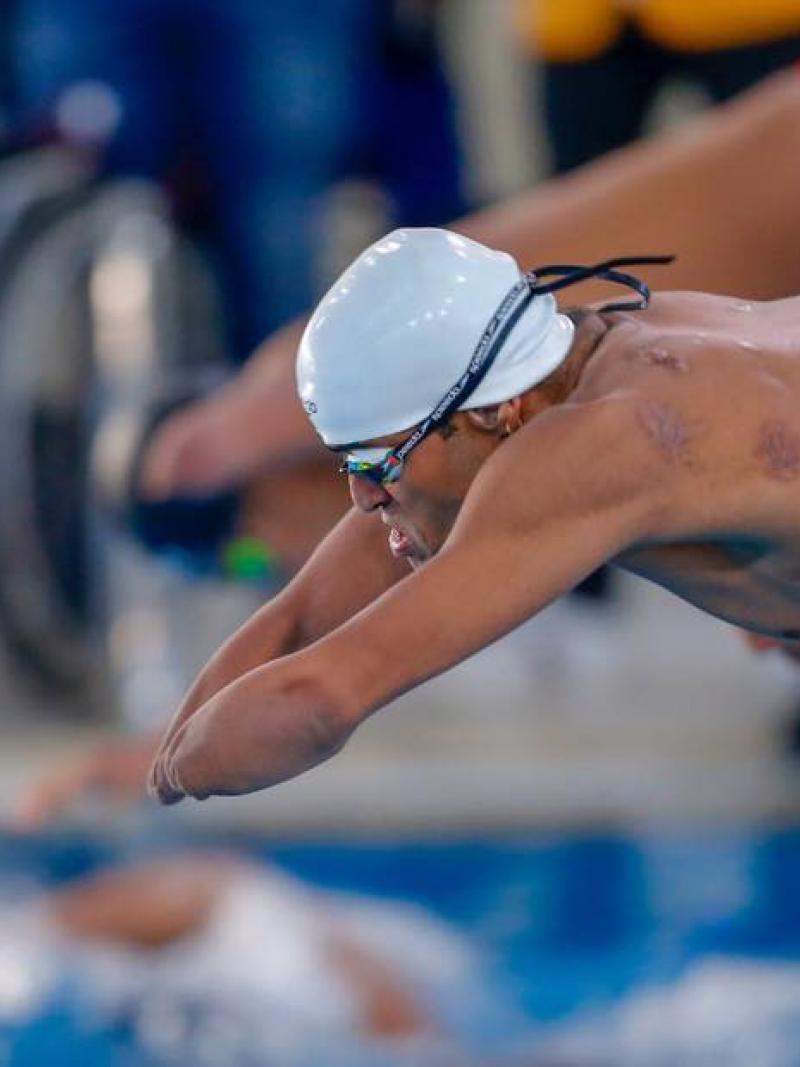 A man without his arms jumping in the swimming pool with another man behind him