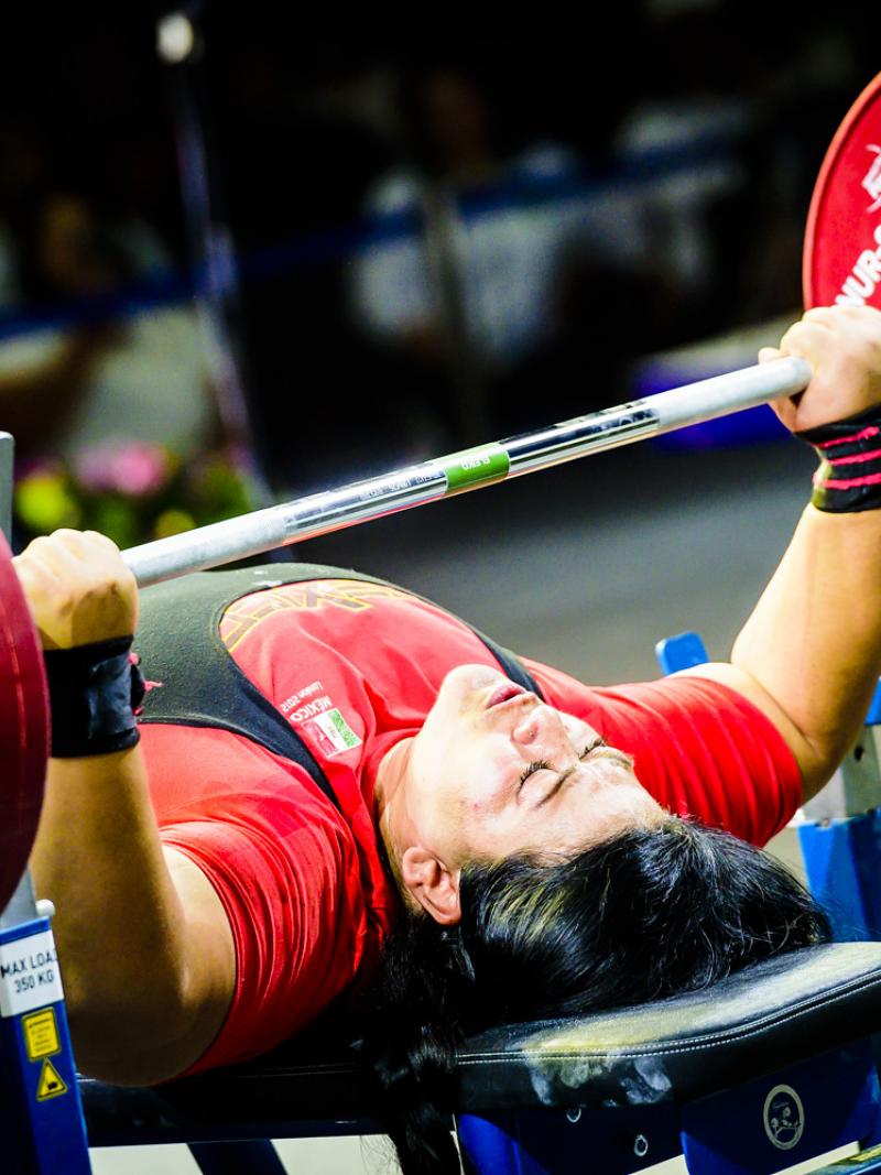 A female powerlifter competing being observed by a man in a chair