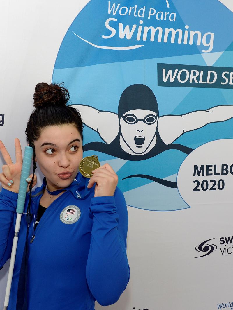 A teenage girl holding a cane and a gold medal while posing for a photo