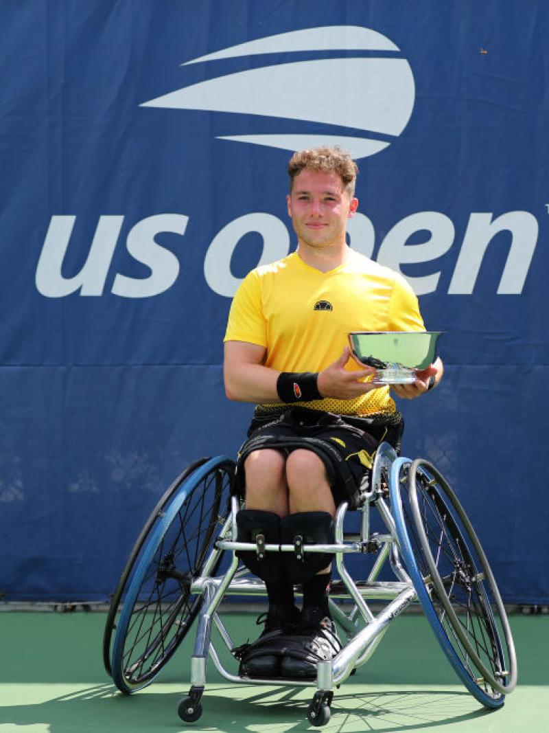British male wheelchair tennis player smiles holding trophy